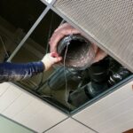 Greenland AC technician installing insulated ductwork above a ceiling